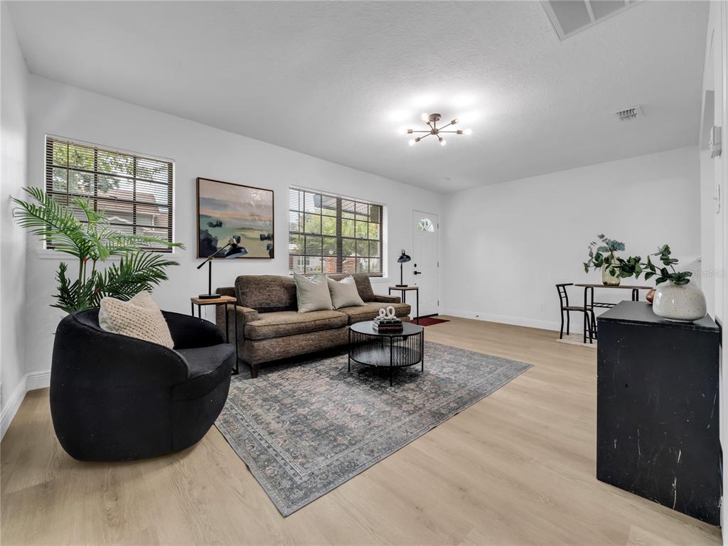 A living room features light wood-look flooring, a brown sofa, a black armchair, and two windows — 14931 FISHER ROAD, TAMPA, FL