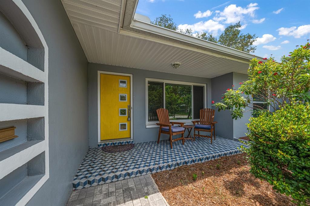 A gray house exterior features a bright yellow front door, patterned tile porch, and chairs — 101 S NEPTUNE AVENUE, CLEARWATER, FL