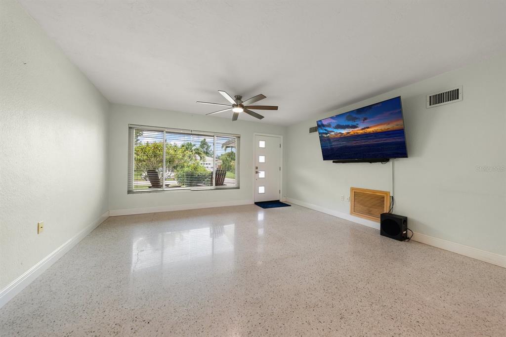 A living room with light walls, a ceiling fan, a large window, and terrazzo flooring — 101 S NEPTUNE AVENUE, CLEARWATER, FL
