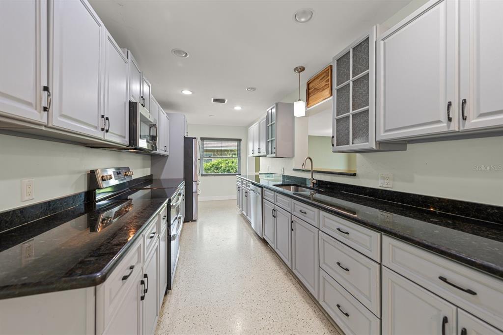A galley kitchen features gray cabinets, dark granite countertops, and light-colored speckled flooring — 101 S NEPTUNE AVENUE, CLEARWATER, FL