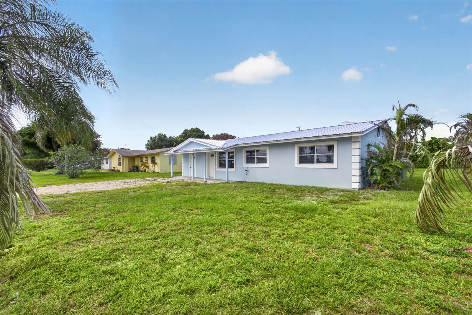 A light blue, single-story house with a metal roof sits on a grassy lot — 15478 SW 150th Street, FL 34956, FL