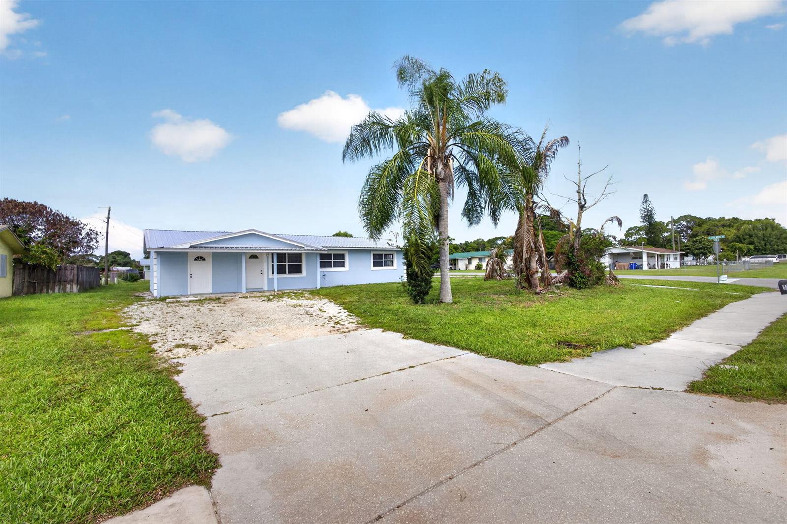 A light blue single-story house features a metal roof, a palm tree, and a driveway — 15478 SW 150th Street, FL 34956, FL