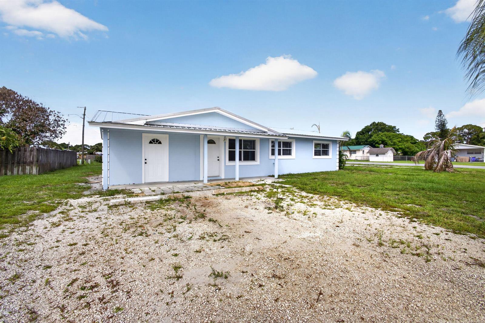 A light blue single-story house with a gravel driveway and a metal roof — 15478 SW 150th Street, FL 34956, FL