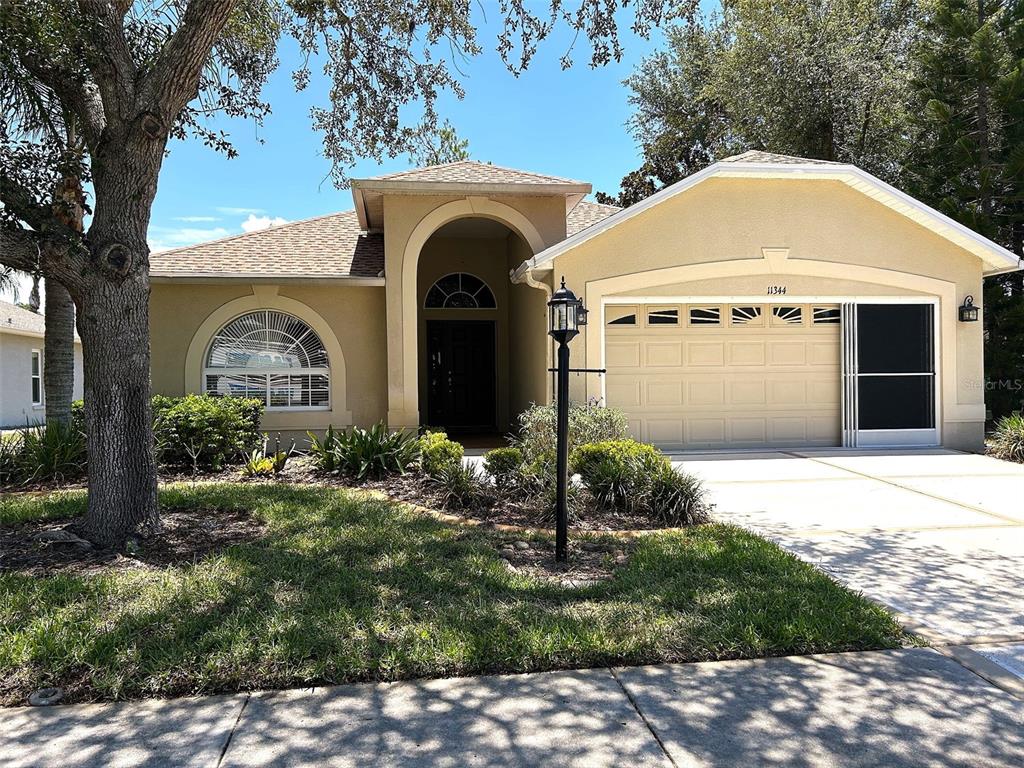 A single-story house with a tan stucco exterior, arched entryway, and a two-car garage — 11344 HERITAGE POINT DRIVE, HUDSON, FL