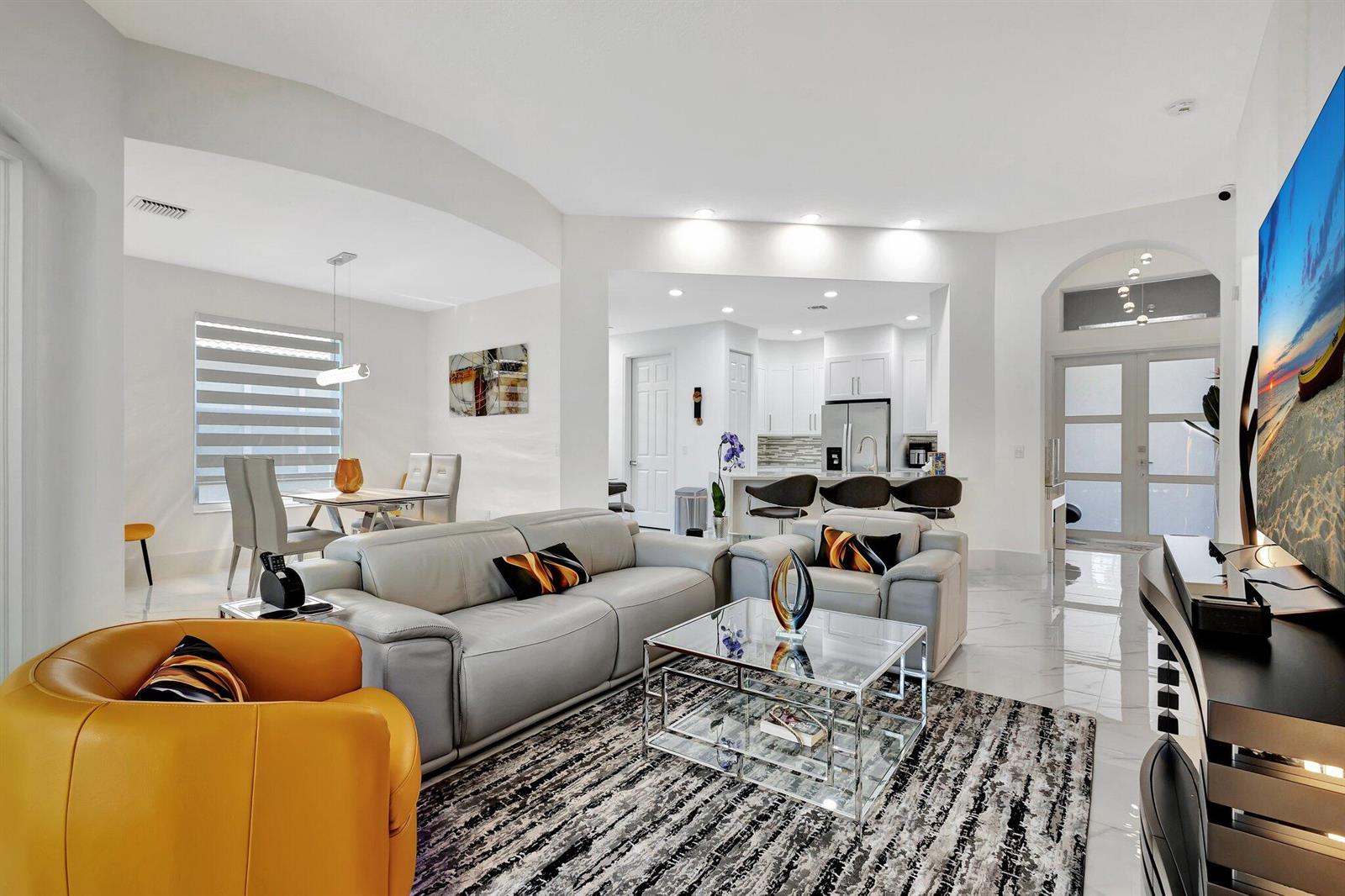 A modern open-concept living room features white tile floors, a grey sofa, and yellow armchair — 6623 Southport Drive, Boynton Beach FL 33472, BOYNTON BEACH, FL