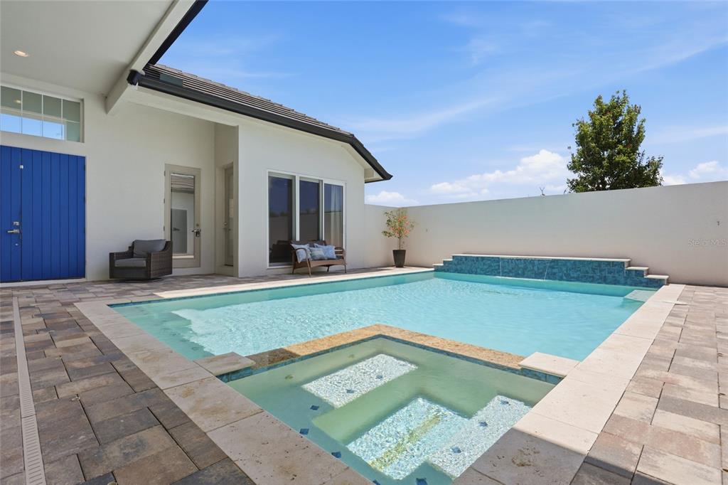 A swimming pool and spa sit on a paved patio beside a modern white house — 2562 HERITAGE GREEN AVENUE, DAVENPORT, FL