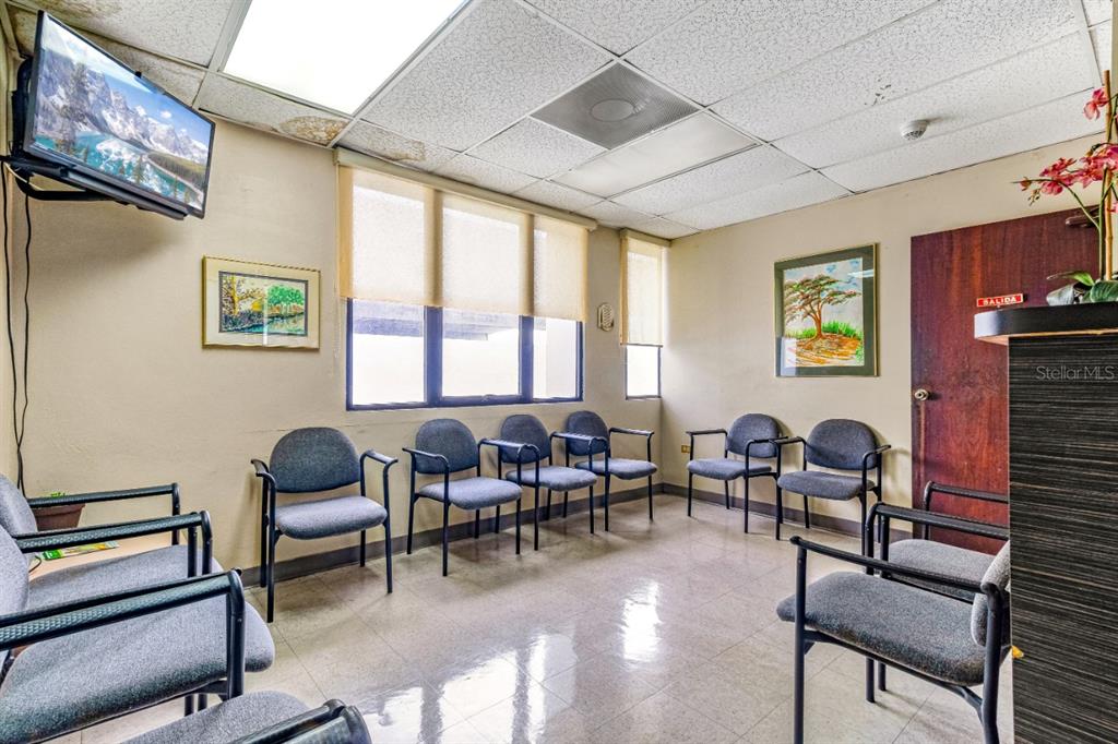 A waiting room with gray chairs, beige walls, a television, and a brown exit door — 506 EDIF. DR.ARTURO CADILLA, BAYAMON, PR
