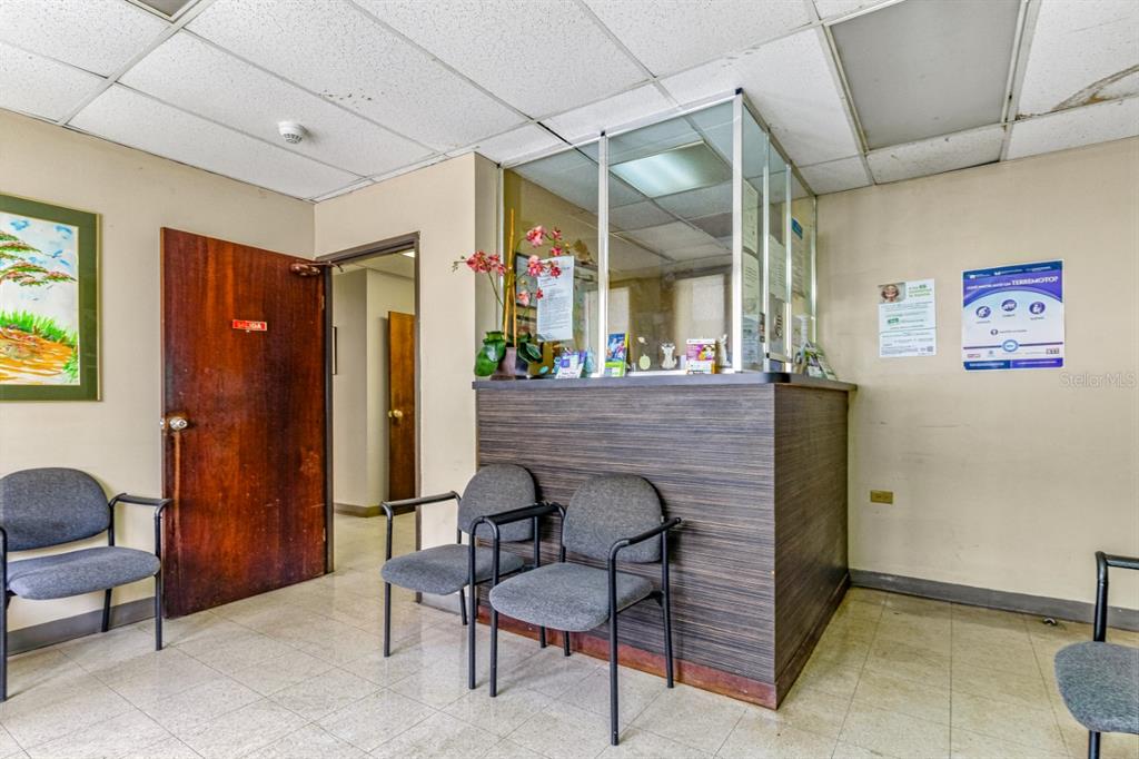 A waiting room features a reception desk, grey chairs, and a wooden door — 506 EDIF. DR.ARTURO CADILLA, BAYAMON, PR