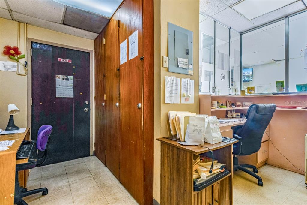 An office space features a dark exit door, wood cabinets, and a desk with chairs — 506 EDIF. DR.ARTURO CADILLA, BAYAMON, PR
