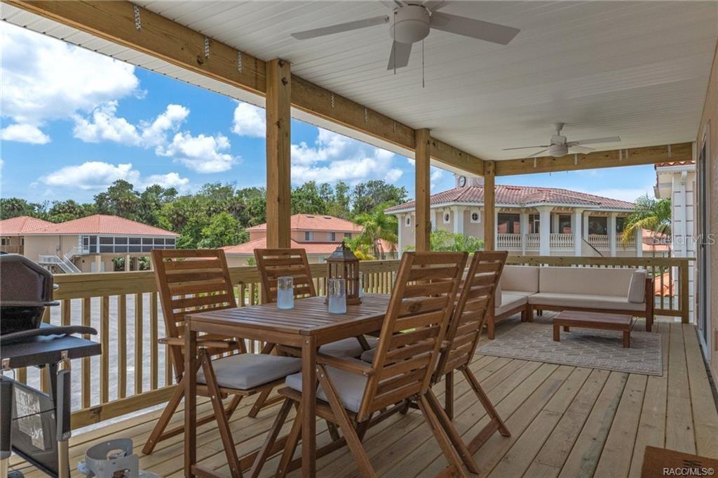A covered wooden deck features a dining set, outdoor sofa, and ceiling fans — 4864 S AMSTEL DRIVE, HOMOSASSA, FL