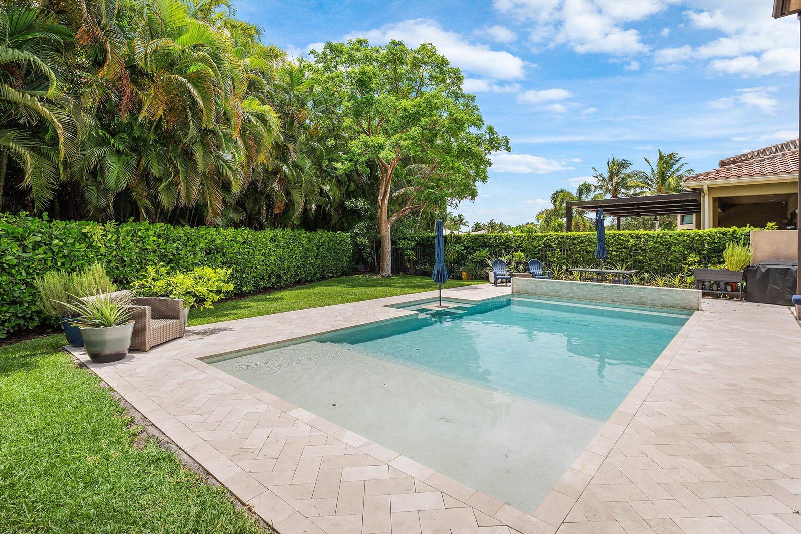 A backyard with a swimming pool, stone patio, green lawn, and lush landscaping — 8658 Lewis River Road, Delray Beach FL 33446, DELRAY BEACH, FL