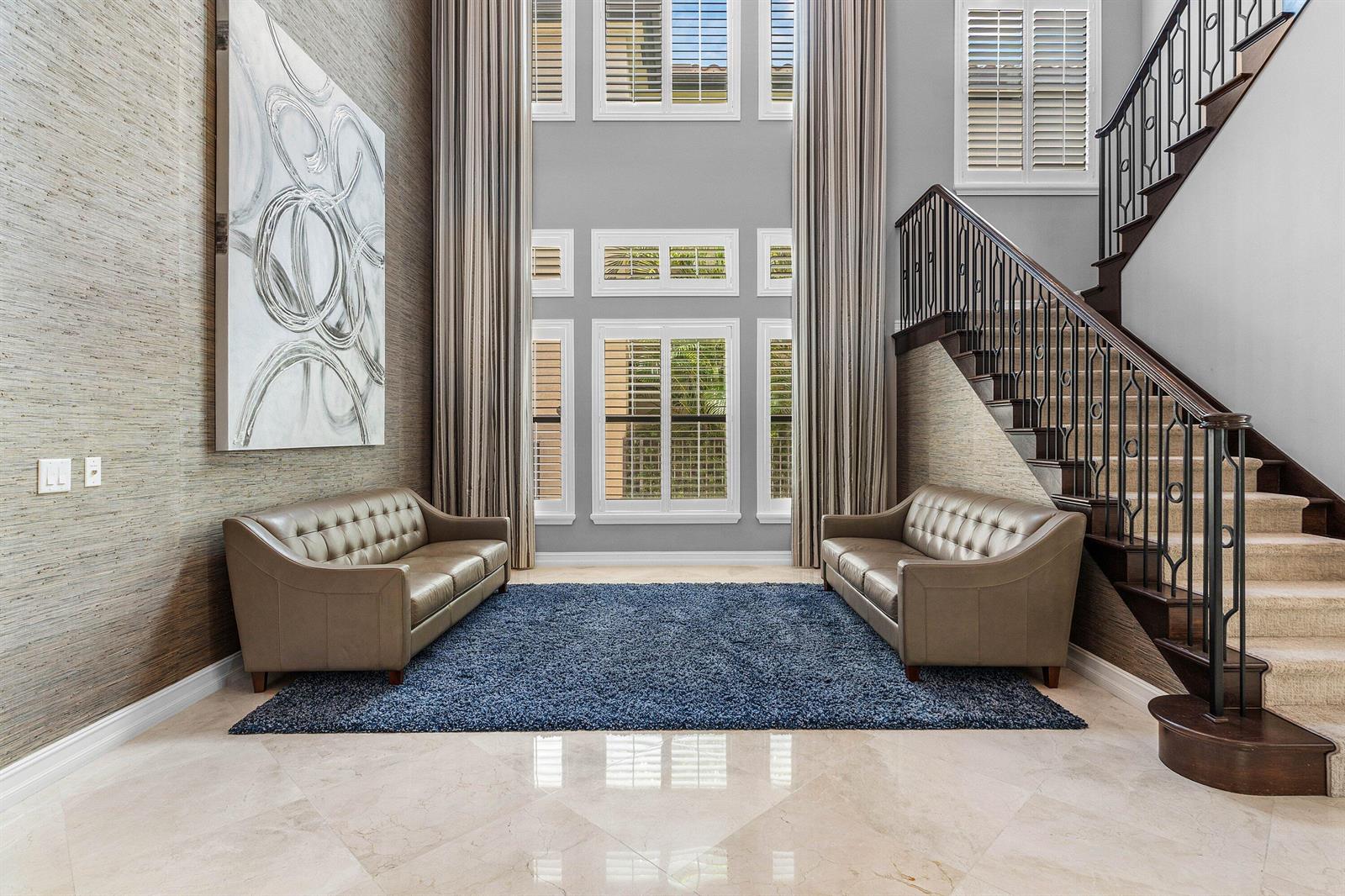 A two-story foyer features two leather sofas, a blue rug, and a staircase with railings — 8658 Lewis River Road, Delray Beach FL 33446, DELRAY BEACH, FL