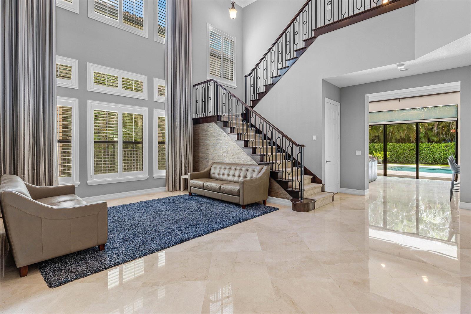 A high-ceilinged living room features a staircase, beige sofas, a blue rug, and marble floors — 8658 Lewis River Road, Delray Beach FL 33446, DELRAY BEACH, FL
