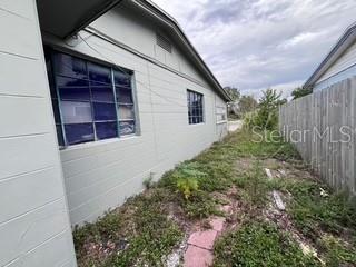 The side exterior of a light-colored house features a grid-patterned window and overgrown landscaping — 4219 5TH AVENUE N, ST PETERSBURG, FL