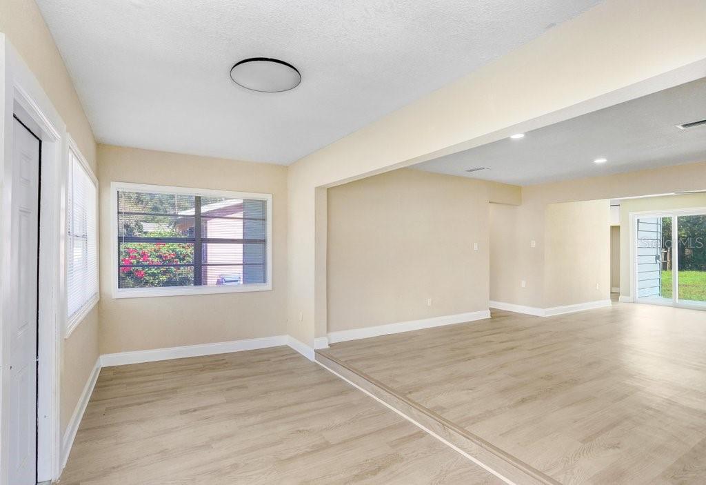 A living area with light wood-look flooring, a step-up transition, and a large window — 10414 RICHARDSON STREET, GIBSONTON, FL