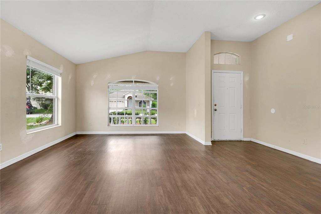 An empty living room features wood-look flooring, beige walls, and a white front door — 1422 LAKE SHORE RANCH DRIVE, SEFFNER, FL