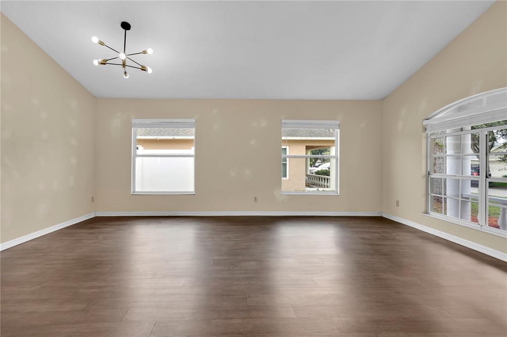 An empty room with light-colored walls, wood-look flooring, a modern chandelier, and three windows — 1422 LAKE SHORE RANCH DRIVE, SEFFNER, FL