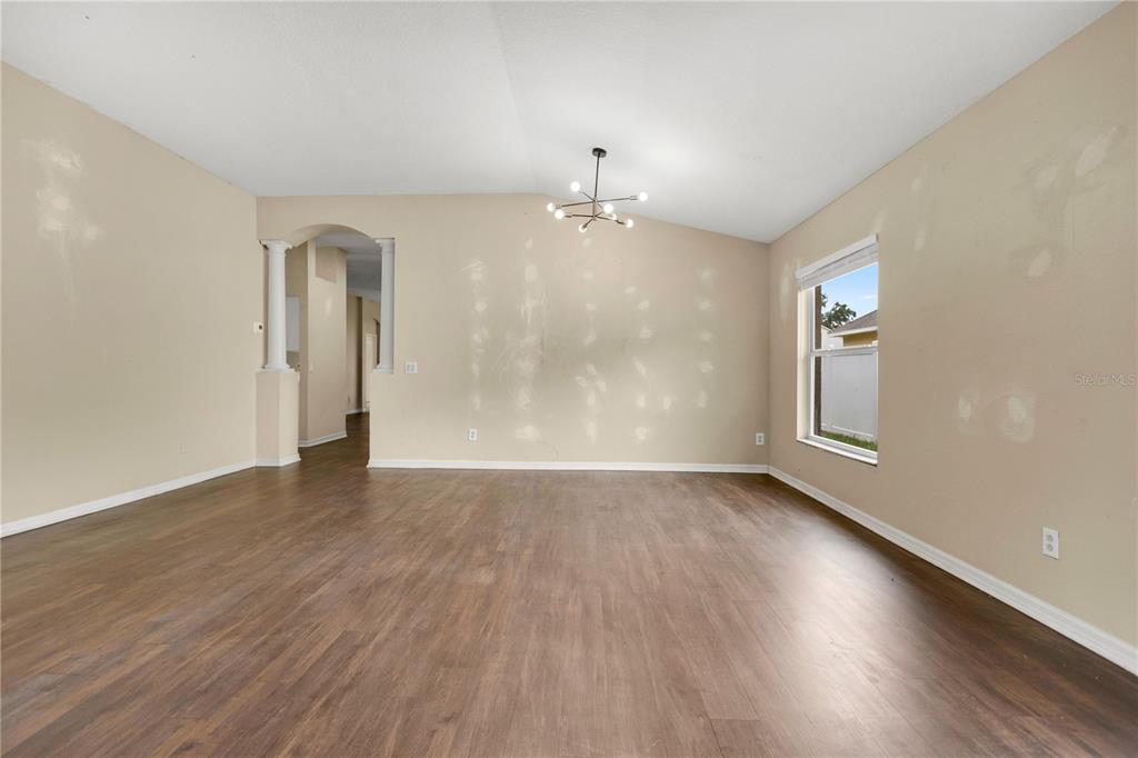 An empty room with beige walls, wood-look flooring, a modern chandelier, and an arched entryway — 1422 LAKE SHORE RANCH DRIVE, SEFFNER, FL