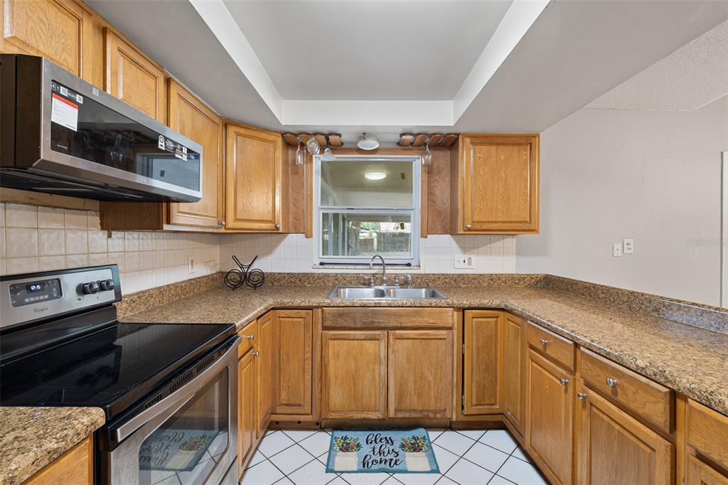 A kitchen features wood cabinets, granite countertops, a stainless steel microwave, and a window — 4035 WENDY DRIVE, ORLANDO, FL