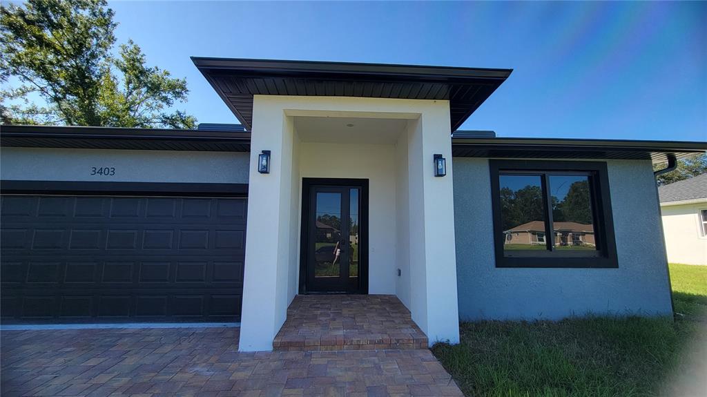 A modern single-story house exterior features a dark garage door, a glass front door, and pavers — 3403 LANGMAID AVENUE, NORTH PORT, FL