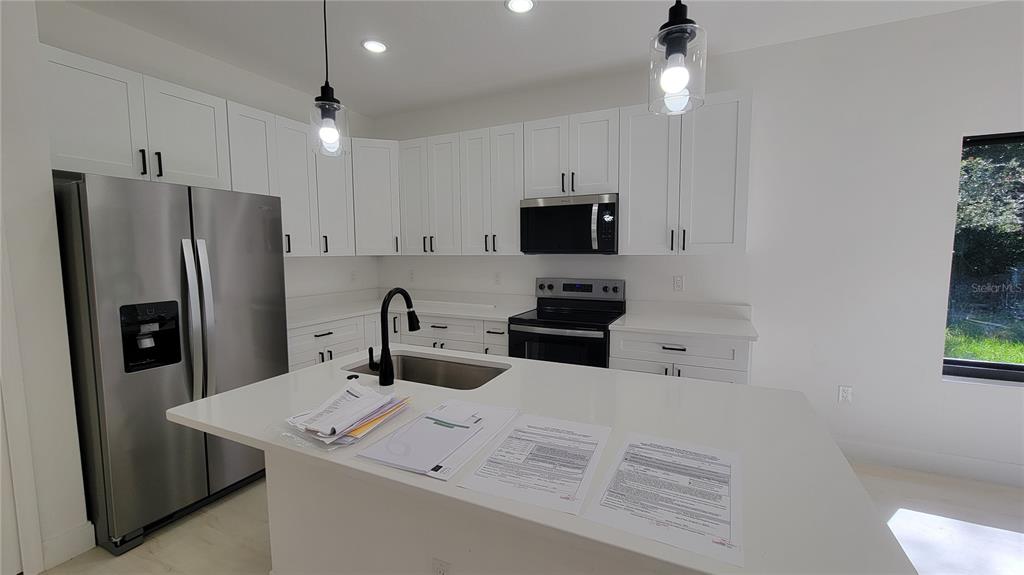 A modern kitchen features white cabinets, stainless steel appliances, and a large central island — 3403 LANGMAID AVENUE, NORTH PORT, FL