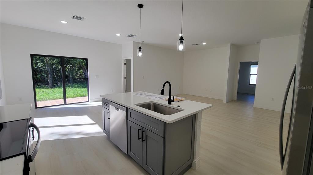 A kitchen island with a sink and pendant lights overlooks a living area with sliding doors — 3403 LANGMAID AVENUE, NORTH PORT, FL