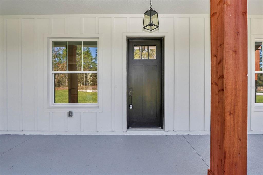 A black front door with a glass pane sits on a porch with white siding — 12886 SW 90 PLACE, DUNNELLON, FL
