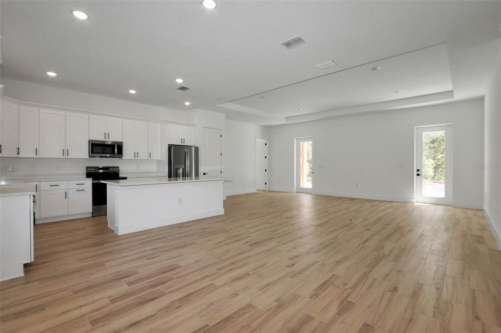 A modern kitchen with white cabinets and a large island opens into a spacious living area — 12886 SW 90 PLACE, DUNNELLON, FL