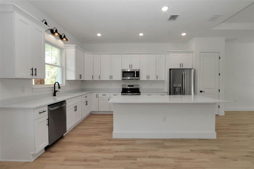 A modern kitchen features white cabinetry, stainless steel appliances, a center island, and light flooring — 12886 SW 90 PLACE, DUNNELLON, FL