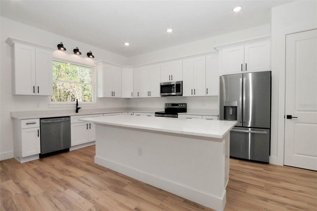A modern kitchen features white cabinetry, stainless steel appliances, a center island, and wood flooring — 12886 SW 90 PLACE, DUNNELLON, FL