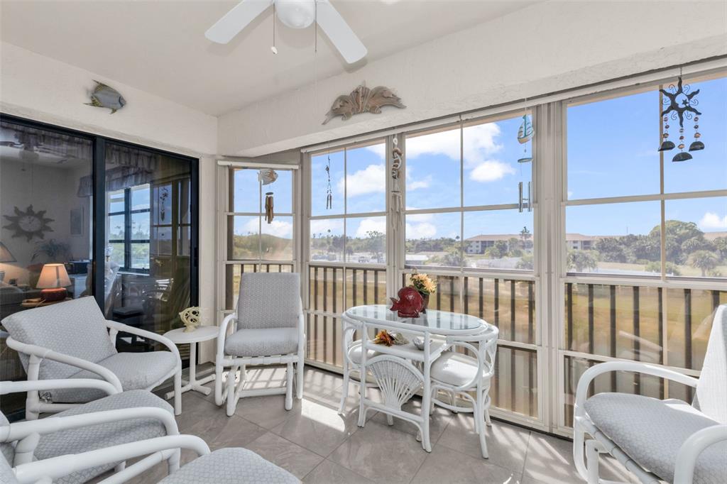 A sunroom features white wicker furniture, tile flooring, and large windows overlooking a grassy landscape — 175 KINGS HIGHWAY UNIT 1032, PUNTA GORDA, FL