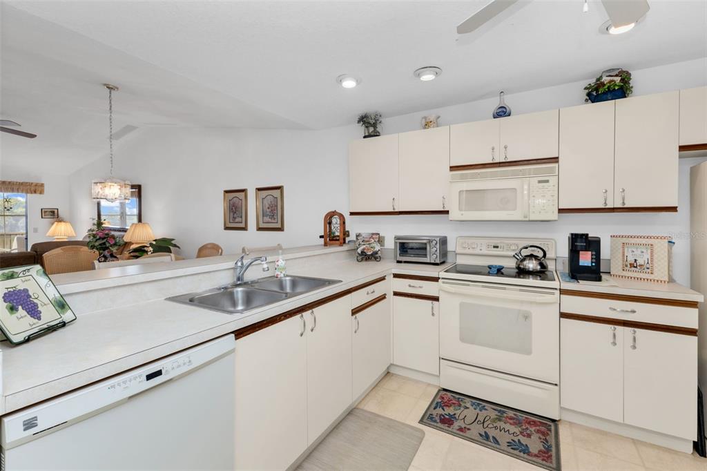 A kitchen with white cabinets, laminate countertops, and a dishwasher opens to a dining area — 175 KINGS HIGHWAY UNIT 1032, PUNTA GORDA, FL