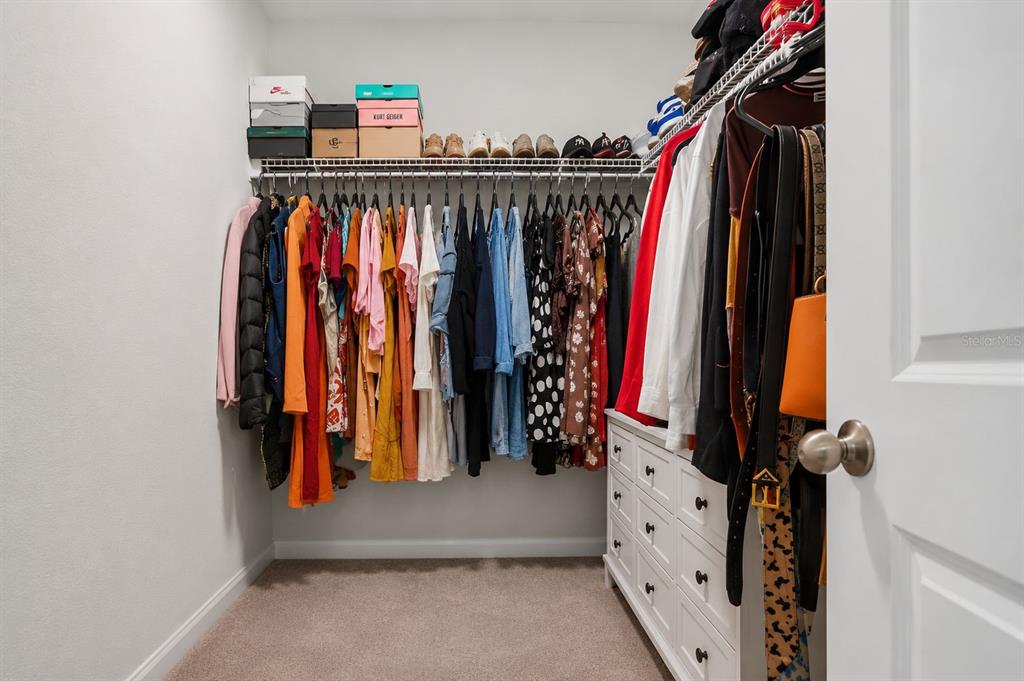 A walk-in closet features a hanging rod with clothes, a top shelf, and white drawers — 1761 PETIOLE PLACE, KISSIMMEE, FL