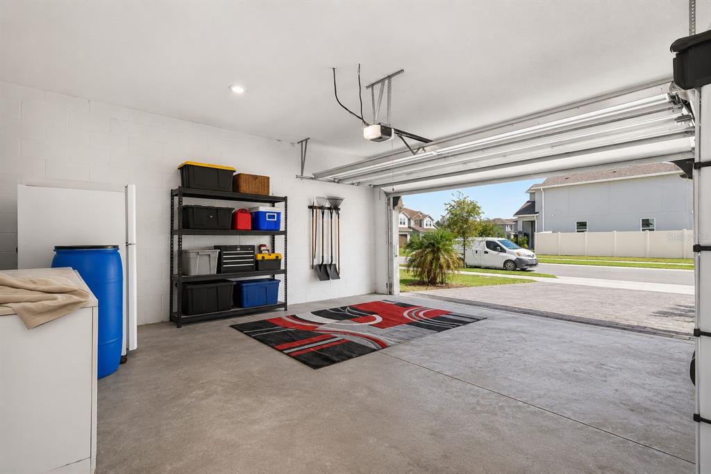 A garage with a concrete floor, storage shelving, a rug, and an open door — 1761 PETIOLE PLACE, KISSIMMEE, FL