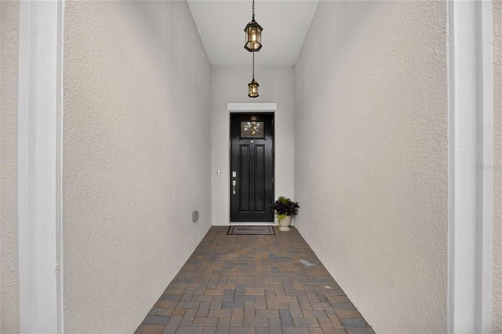 A covered entryway features a black front door, brick paver flooring, and two hanging lanterns — 17219 SCUBA CREST STREET, WIMAUMA, FL