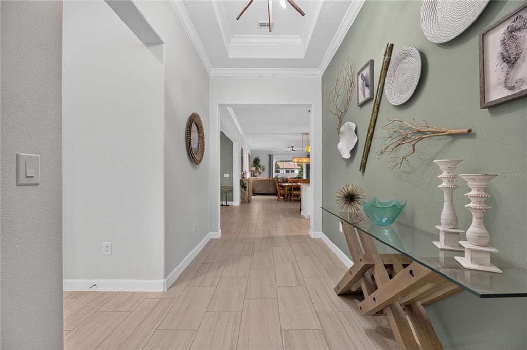 A hallway with light tile floors leads to an open living area with tray ceilings — 17219 SCUBA CREST STREET, WIMAUMA, FL