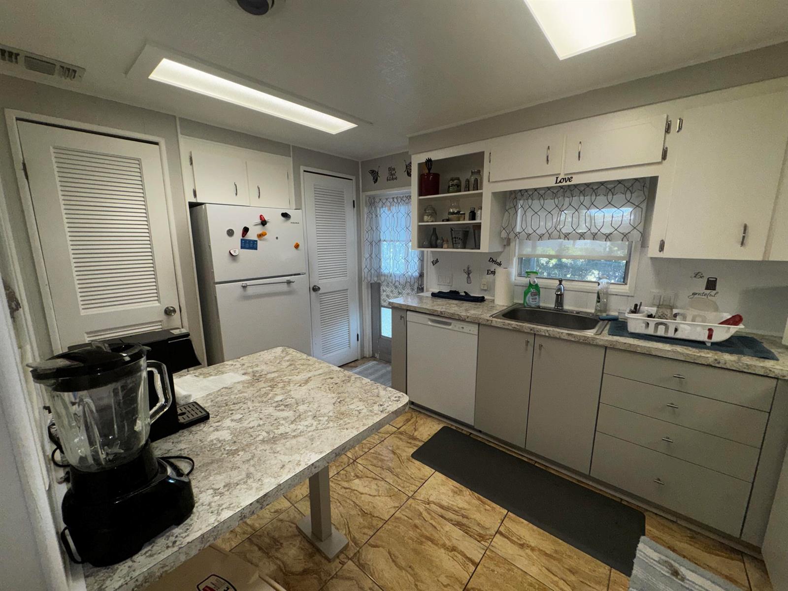 A kitchen features white cabinets, a stone-patterned island, stainless steel sink, and tiled flooring — 4242 3rd Court, Lantana FL 33462, LANTANA, FL