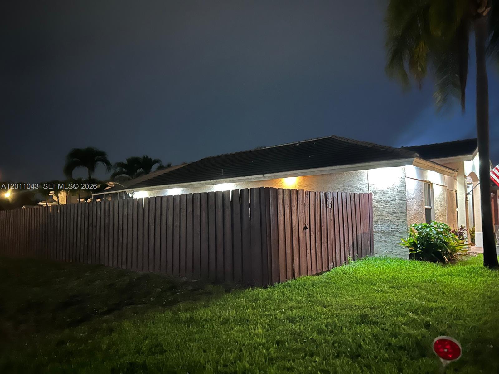 A dark wooden fence surrounds the side of a house at night — 18516 NW 56th Ave, Miami Gardens FL 33055, MIAMI GARDENS, FL