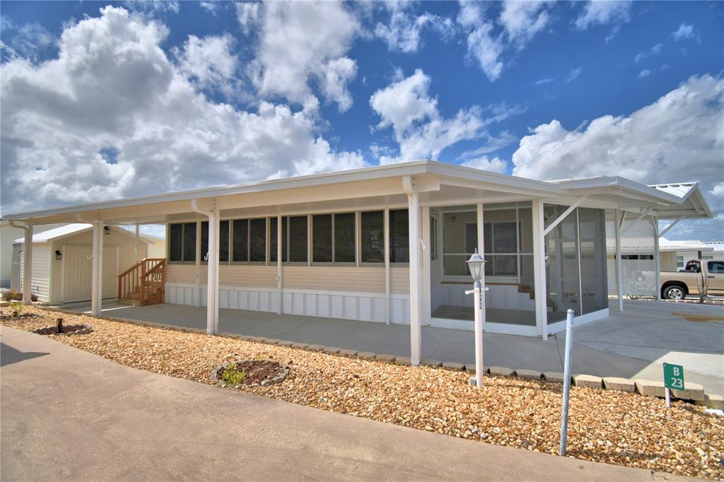 A manufactured home features a long covered carport, a screened-in porch, and a gravel yard — 251 PATTERSON ROAD UNIT B23, HAINES CITY, FL