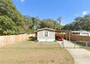 A single-story manufactured home with a carport and a fenced yard under a blue sky — 4422 STILLMAN STREET, ZEPHYRHILLS, FL