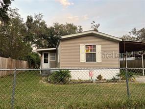 A single-story manufactured home with tan siding and a chain-link fence in the front yard — 4422 STILLMAN STREET, ZEPHYRHILLS, FL