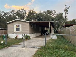 A single-story manufactured home features light siding, a metal carport, and a chain-link fence — 4422 STILLMAN STREET, ZEPHYRHILLS, FL