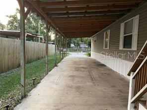 A concrete carport with a wooden roof structure sits beside a house with gray siding — 4422 STILLMAN STREET, ZEPHYRHILLS, FL