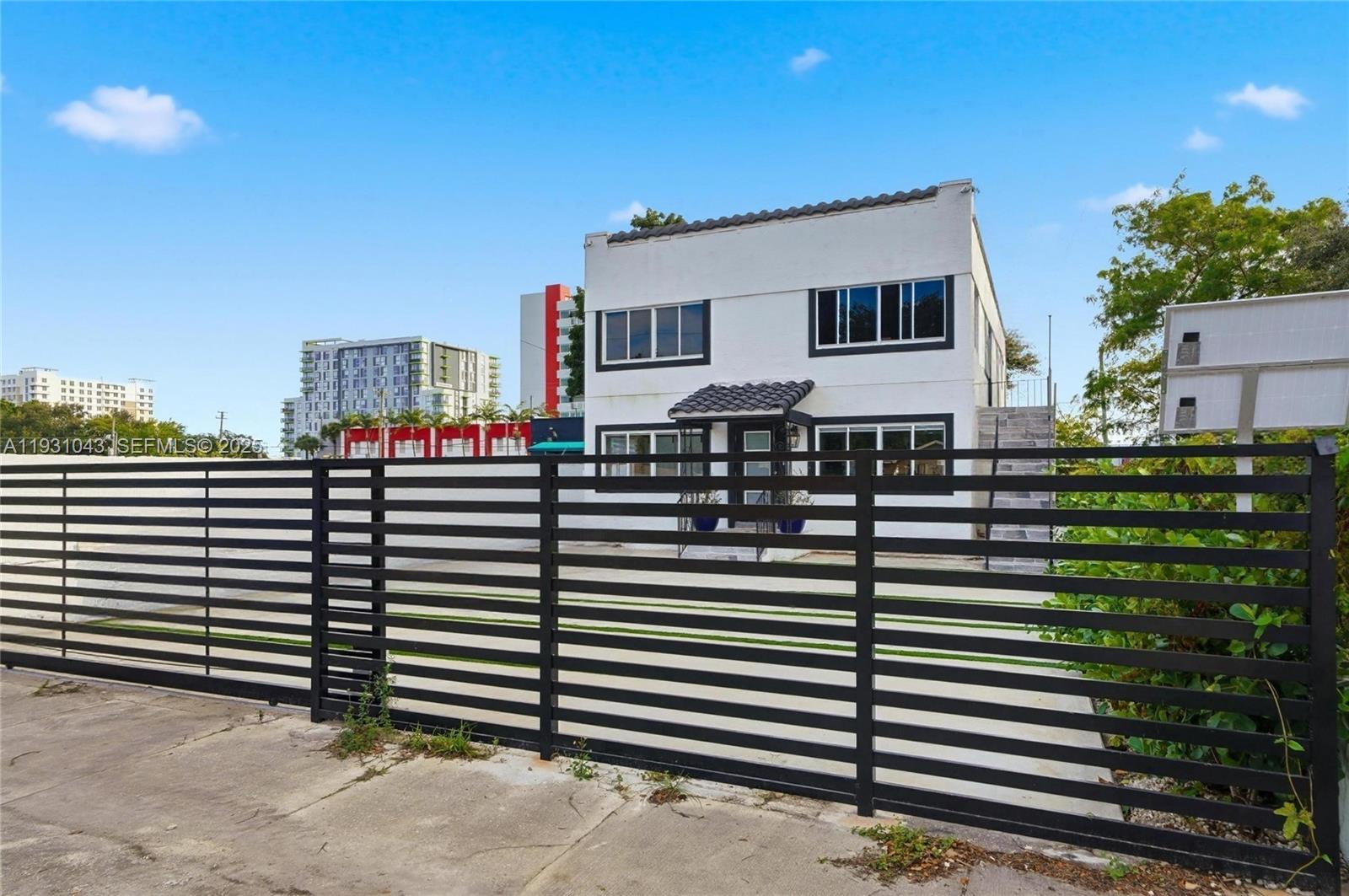 A two-story white building with dark-framed windows stands behind a black horizontal slat fence — 1590 NW 38th St # 1, Miami FL 33142, MIAMI, FL