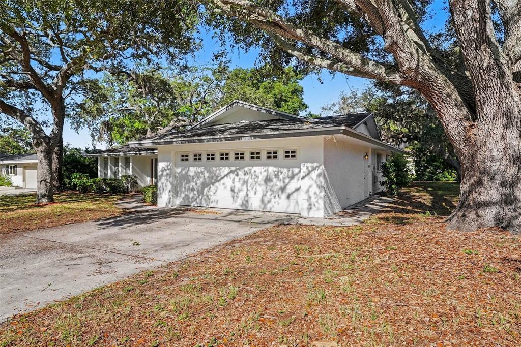A white house with a two-car garage sits under large trees on a sunny day — 209 15TH STREET, PALM HARBOR, FL