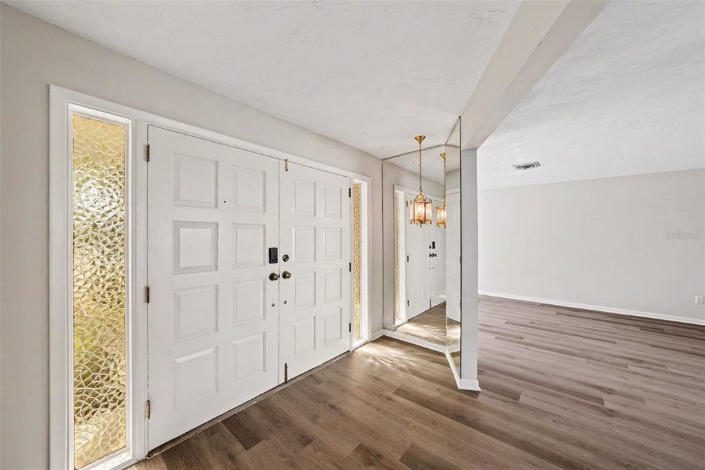 An entryway features double white doors, wood-look flooring, and a mirrored wall with hanging lights — 209 15TH STREET, PALM HARBOR, FL