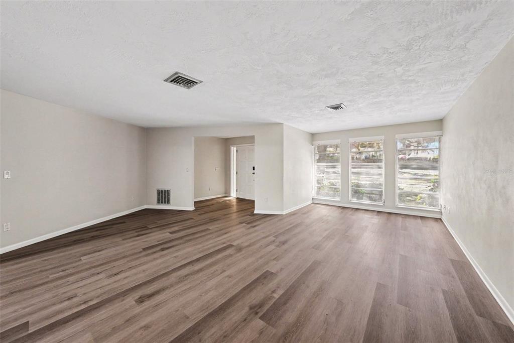 An empty living room features light gray walls, wood-look flooring, and three large windows — 209 15TH STREET, PALM HARBOR, FL