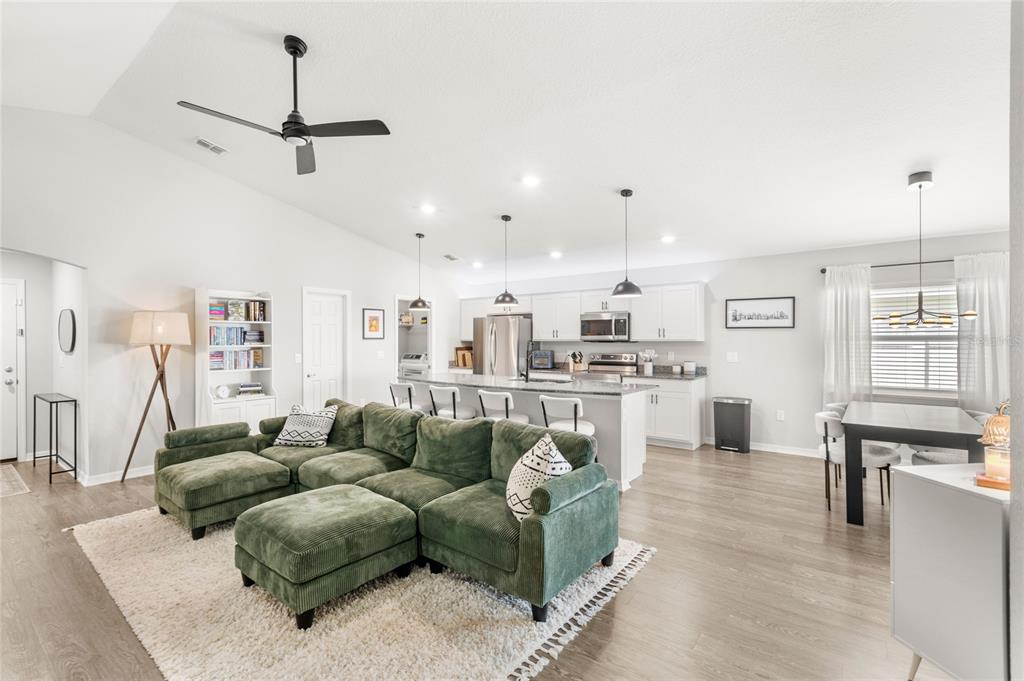 An open-concept living room and kitchen featuring a green sectional sofa and white cabinetry — 4215 SWAN STREET, HAINES CITY, FL