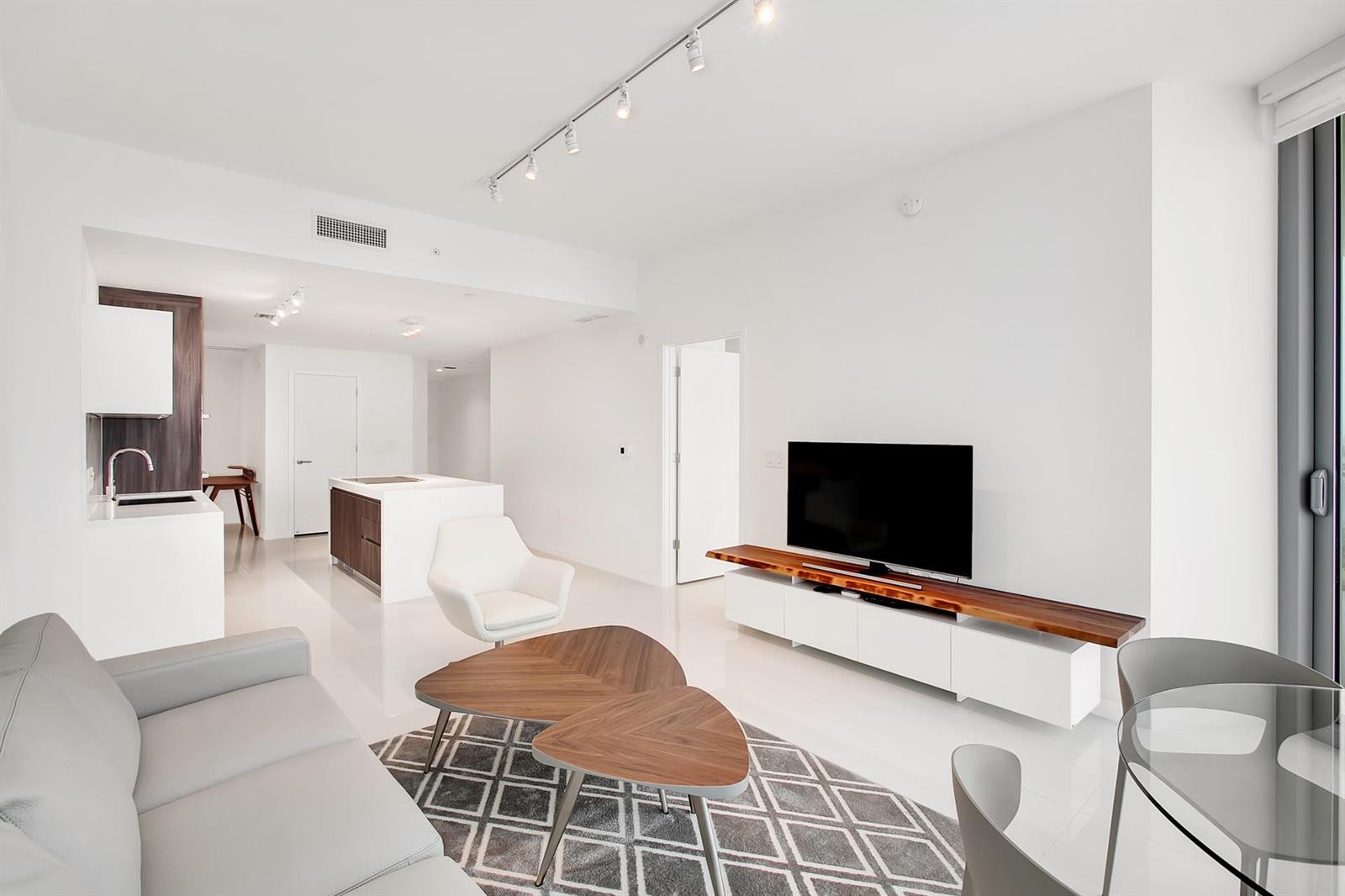 A modern living room with white floors, a wooden coffee table, and a television console — 851 NE 1st Avenue # 2005, Miami FL 33132, MIAMI, FL