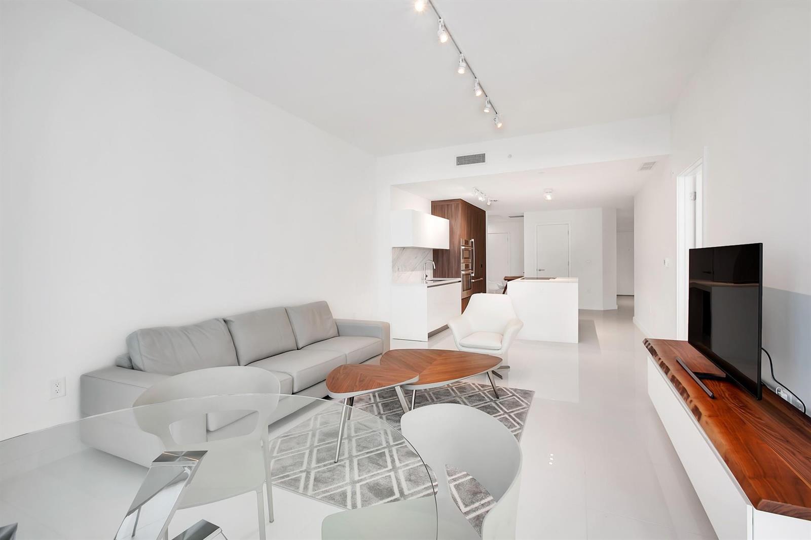 A modern living room with a gray sofa, wood coffee tables, and an open kitchen — 851 NE 1st Avenue # 2005, Miami FL 33132, MIAMI, FL
